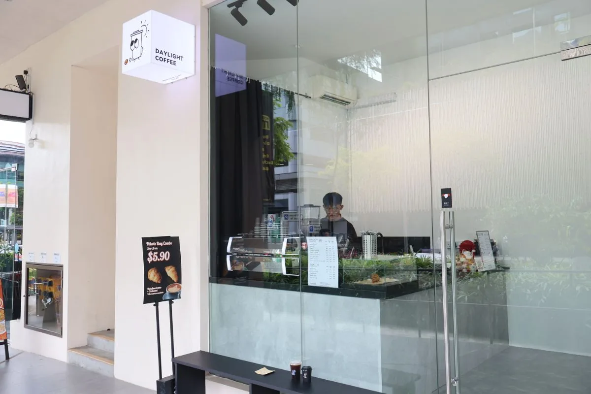 The Daylight Coffee takeaway kiosk behind glass at Hotel Mi Bencoolen, lightbox sign above the counter